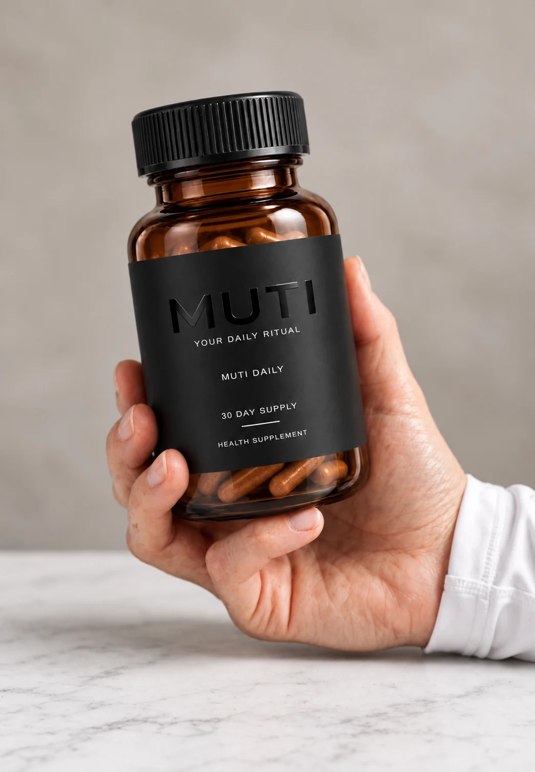 A hand holding the amber MUTI DAILY bottle above a pale stone counter